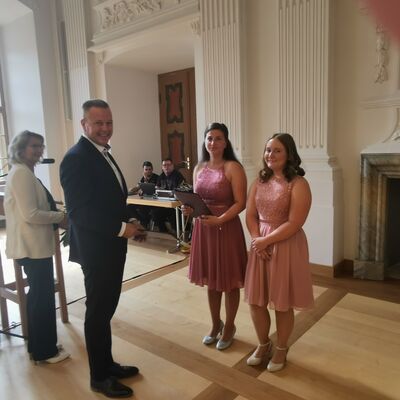 Ausbildungsleiterin Silke Flohr und Bürgermeister Bernhard Hiebe überreichen die Abschlusszeugnisse an Leonie Hahne und Saskia Speer.